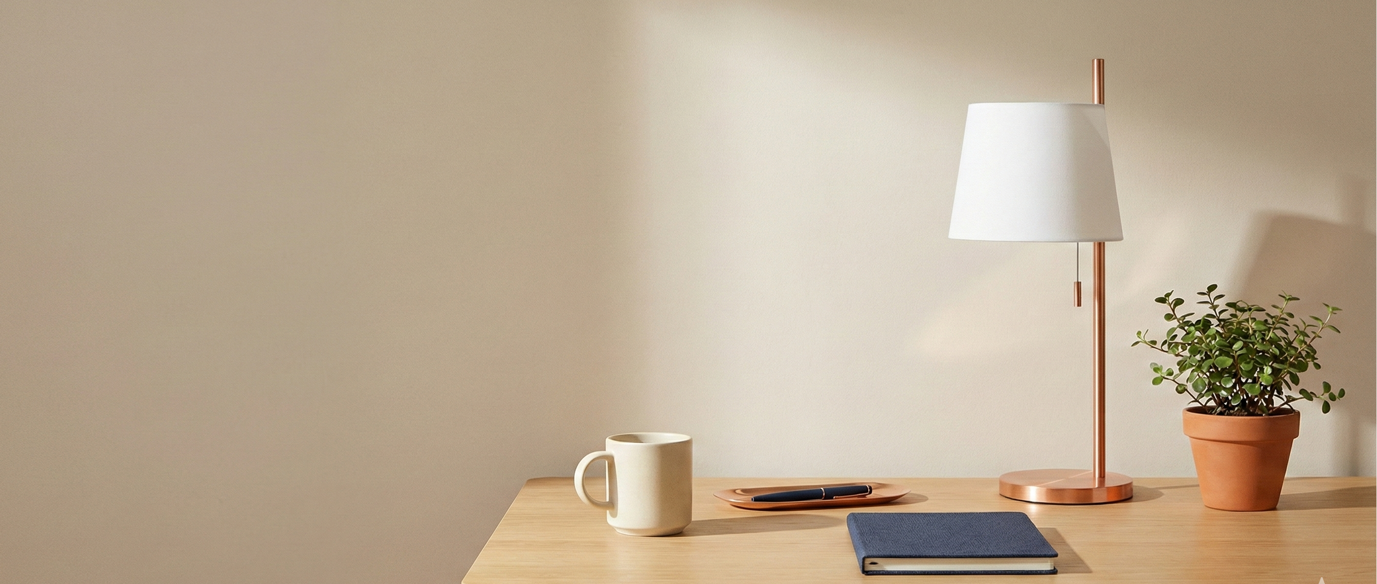 Wooden desk with a lamp, mug, and plant against a beige wall