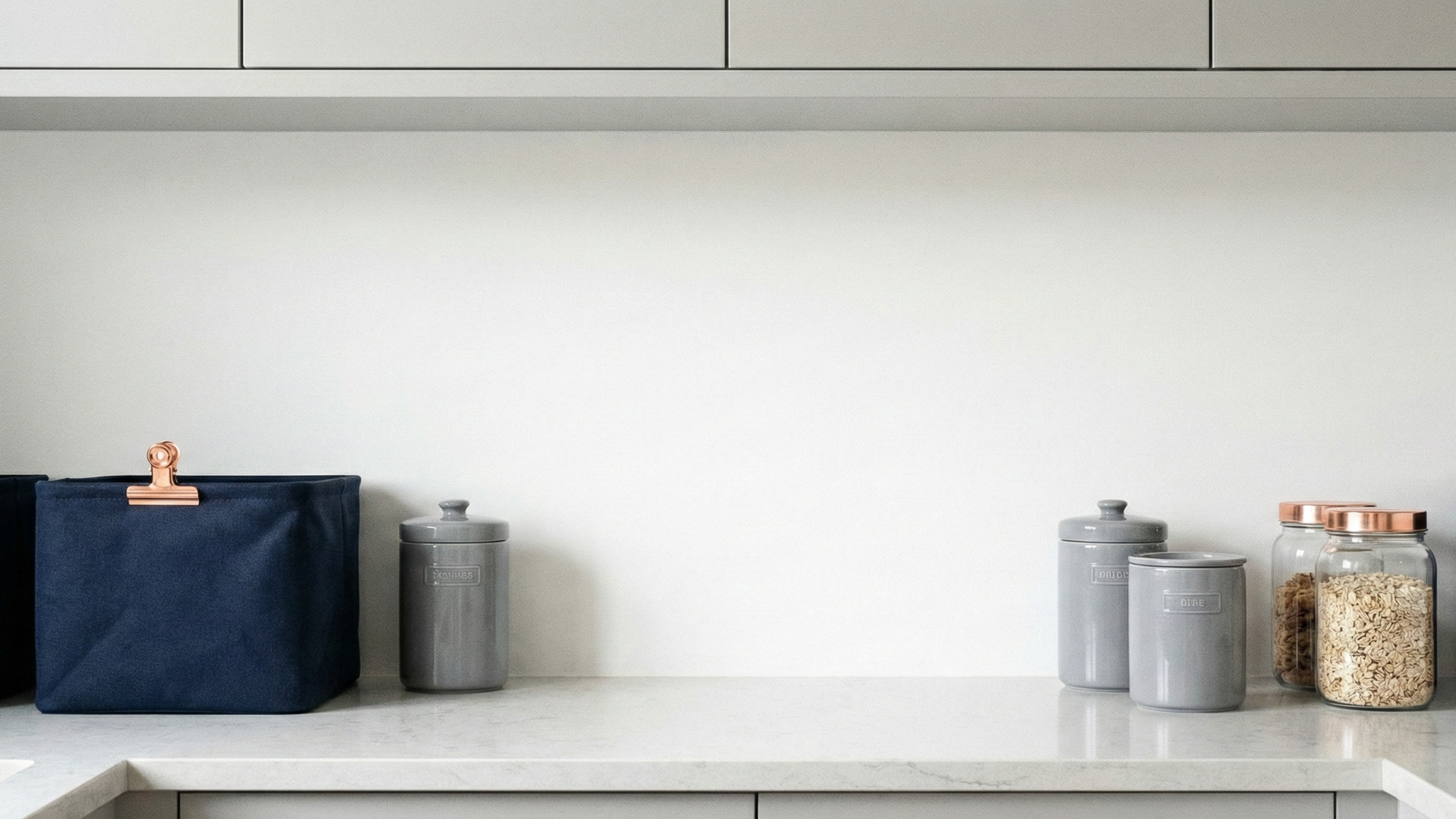 Kitchen counter with a navy blue bag and gray canisters against a white wall.