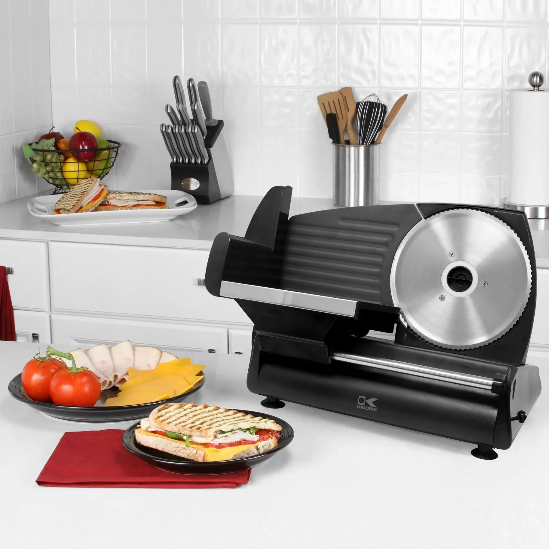 Black meat slicer on a kitchen counter with food items and utensils in the background.